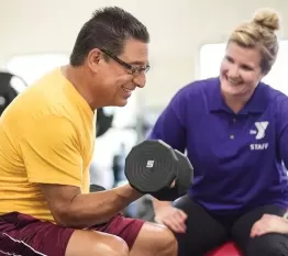 YMCA staff helping man with weightlifting